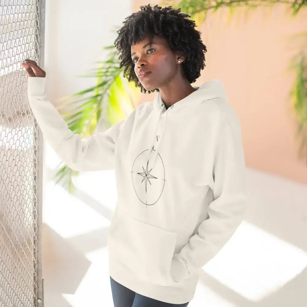 Woman modeling a cream-colored Cozy Compass Unisex Hoodie with adjustable hood and low heat fleece for travel and casual wear