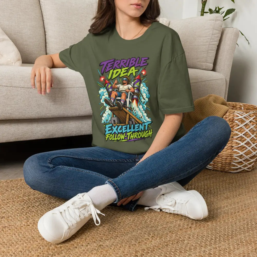 Olive green oversized unisex t-shirt with retro rocket graphic and text terrible idea excellent follow-through low heat tumble dry care instructions